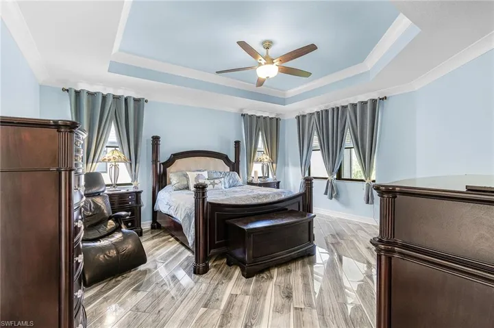 Bedroom featuring wood finish floors, ceiling fan, crown molding, and a tray ceiling