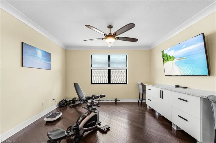Exercise area featuring dark wood-style flooring, ornamental molding, and ceiling fan