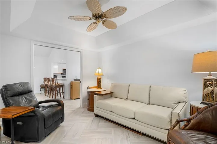 Living room featuring a tray ceiling, ceiling fan, and parquet floors