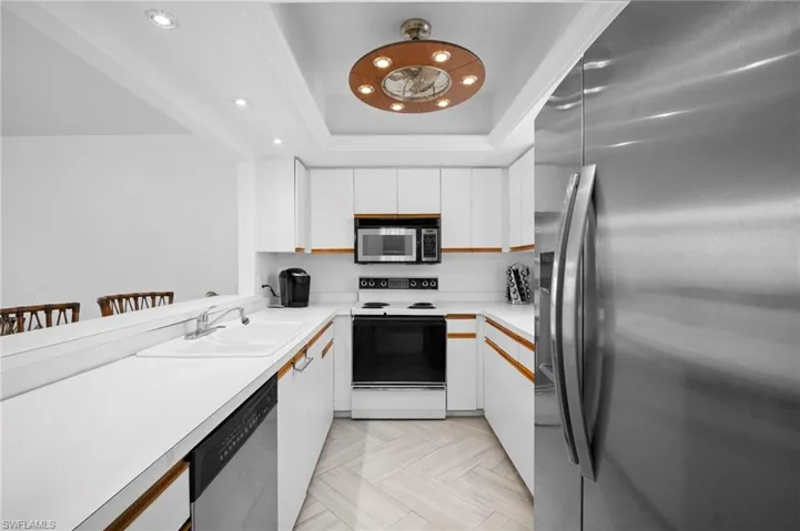 Dual tone kitchen featuring stainless steel appliances, light countertops, a raised ceiling, a kitchen bar, and recessed lighting