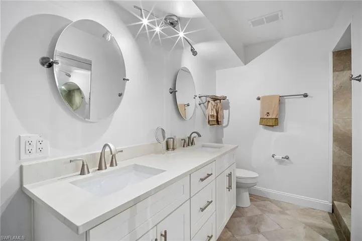 Bathroom with double vanity, tiled shower, and light tile patterned floors