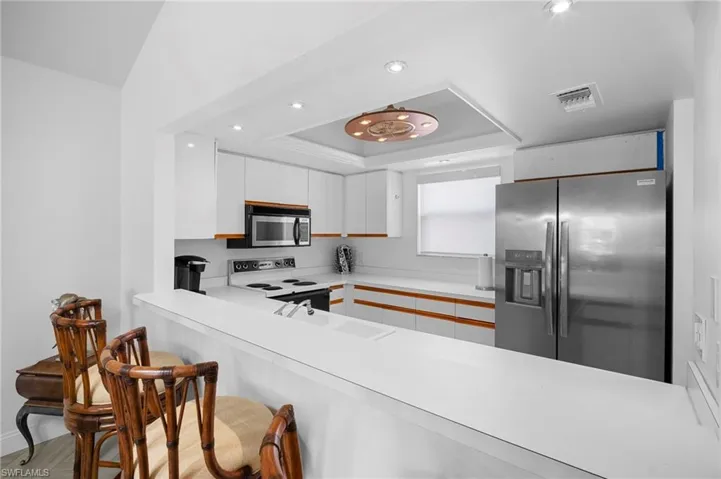 Kitchen with light countertops, stainless steel appliances, a breakfast bar, a raised ceiling, and recessed lighting
