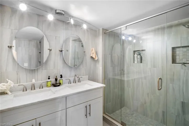 Full bathroom with double vanity, a stall shower, and tile walls
