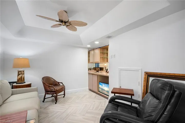 Living area with a tray ceiling, ceiling fan, parquet floors, wet bar, and recessed lighting