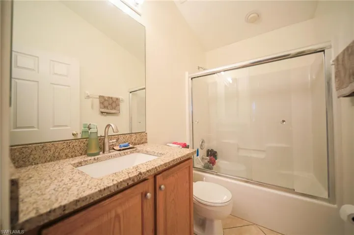 Full bath with tile patterned flooring, vanity, enclosed tub / shower combo, and vaulted ceiling