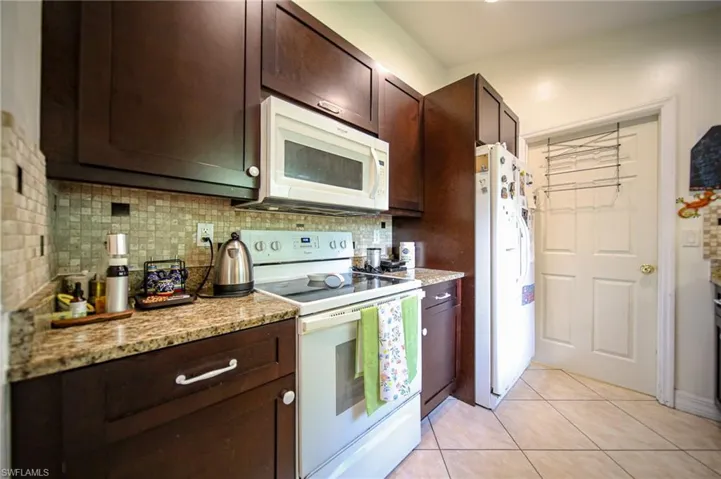 Kitchen featuring white appliances, backsplash, and dark brown cabinetry