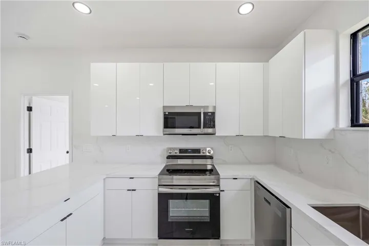 Kitchen with appliances with stainless steel finishes, white cabinets, light stone countertops, recessed lighting, and modern cabinets