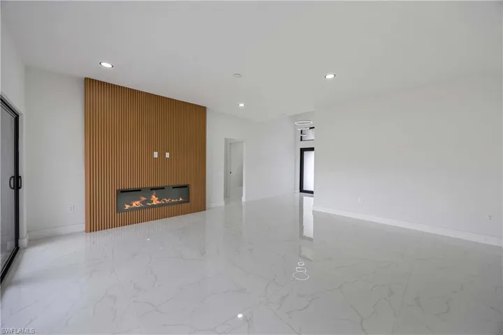 Empty room with marble finish flooring, recessed lighting, a glass covered fireplace, and baseboards