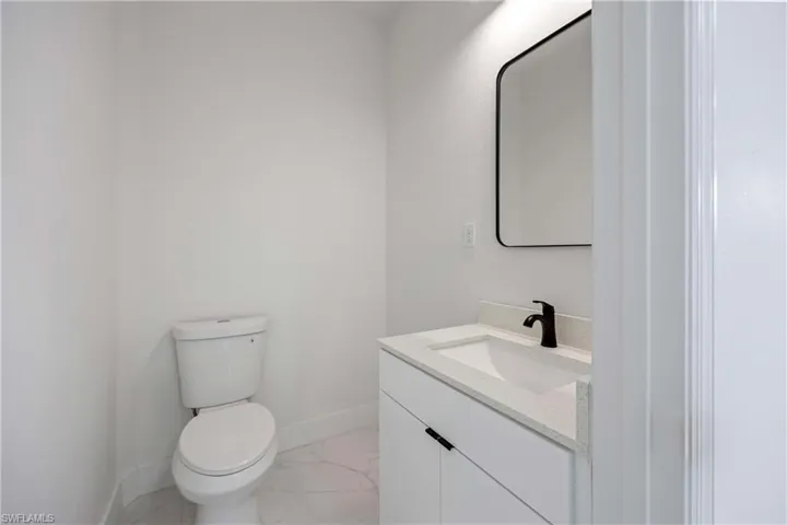 Half bath featuring baseboards, marble look tiles, vanity, and toilet