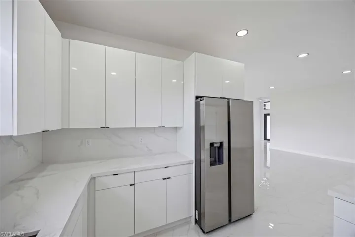 Kitchen with stainless steel refrigerator with ice dispenser, light marble finish floors, white cabinets, modern cabinets, and recessed lighting