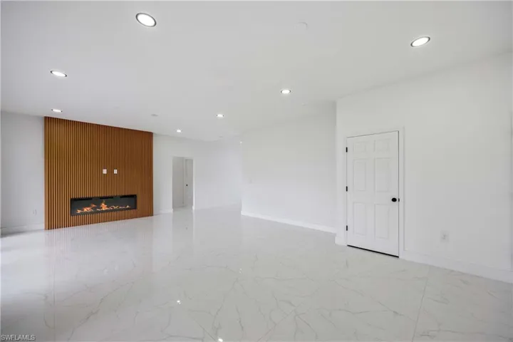 Empty room with recessed lighting, light marble finish flooring, baseboards, and a glass covered fireplace