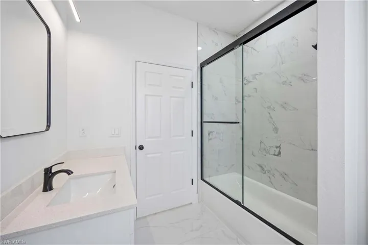 Bathroom with combined bath / shower with glass door, vanity, and marble finish floors