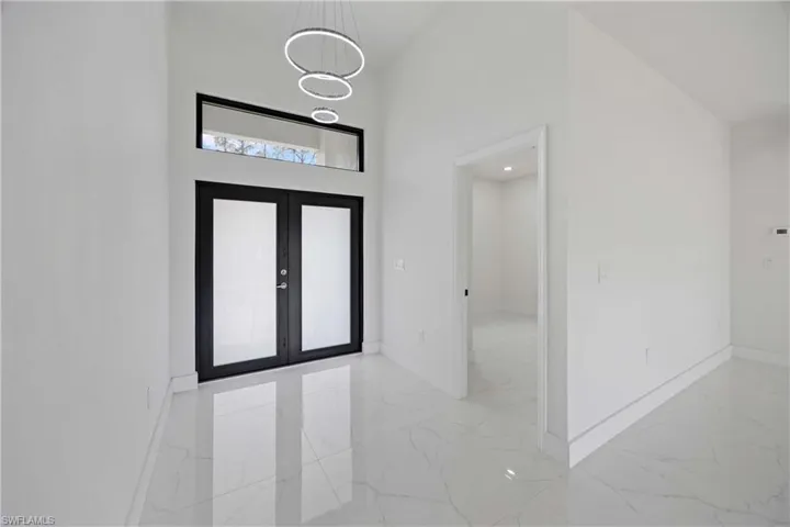 Entrance foyer featuring light marble finish flooring, baseboards, a high ceiling, and french doors