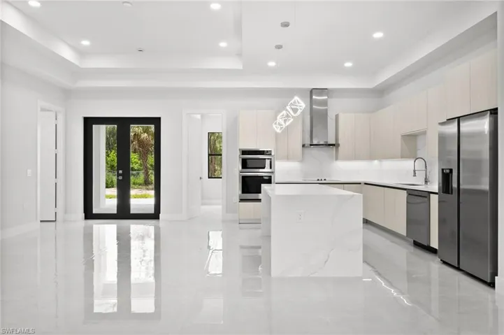 Kitchen with stainless steel appliances, modern cabinets, wall chimney exhaust hood, a raised ceiling, and recessed lighting
