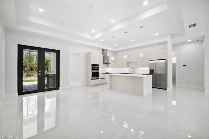 Kitchen featuring modern cabinets, appliances with stainless steel finishes, wall chimney exhaust hood, a raised ceiling, and a center island