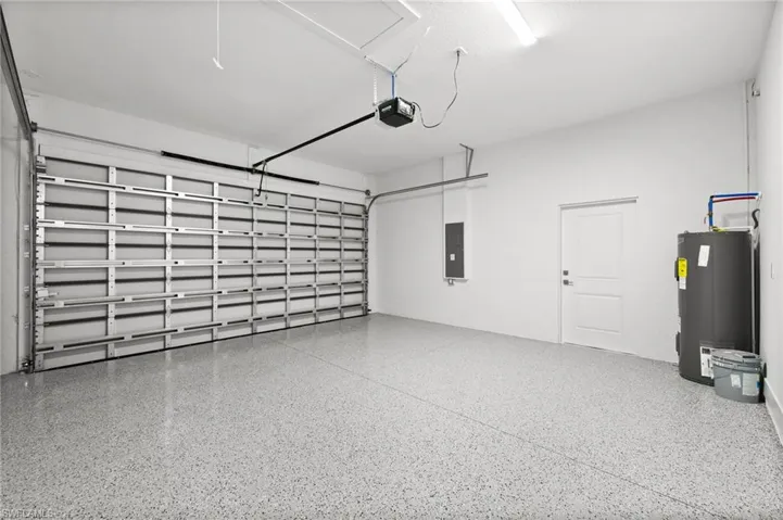 Garage featuring electric water heater, electric panel, and a garage door opener
