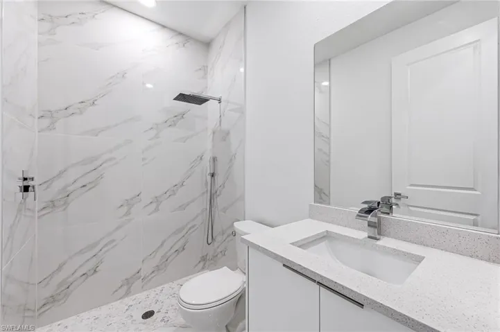 Bathroom with a tile shower, vanity, and toilet
