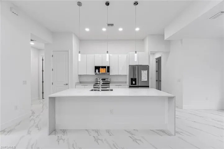 Kitchen with a center island with sink, pendant lighting, white cabinetry, and stainless steel appliances