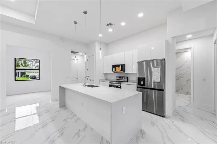 Kitchen featuring decorative light fixtures, sink, stainless steel appliances, an island with sink, and white cabinets