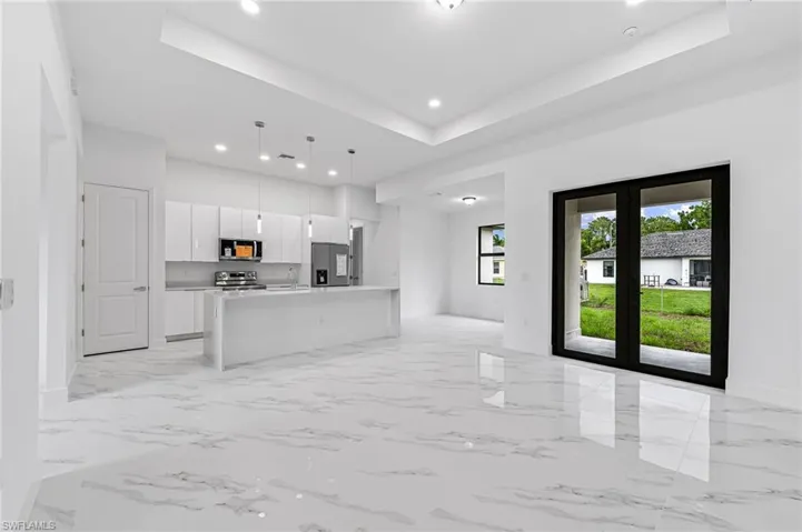 Kitchen featuring a kitchen island with sink, a raised ceiling, decorative light fixtures, stainless steel appliances, and white cabinetry