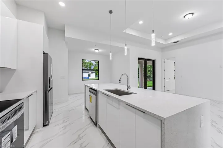 Kitchen with hanging light fixtures, plenty of natural light, white cabinetry, and sink