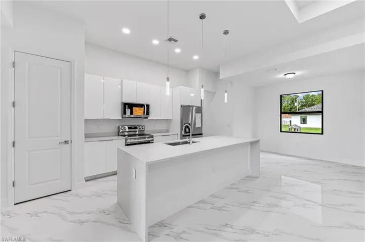 Kitchen with a kitchen island with sink, sink, stainless steel appliances, hanging light fixtures, and white cabinetry
