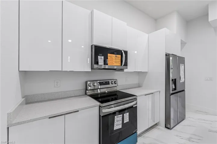 Kitchen featuring white cabinets, appliances with stainless steel finishes, and light stone countertops
