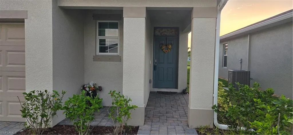 Covered entry with a paver walkway, stucco exterior, and accent trim