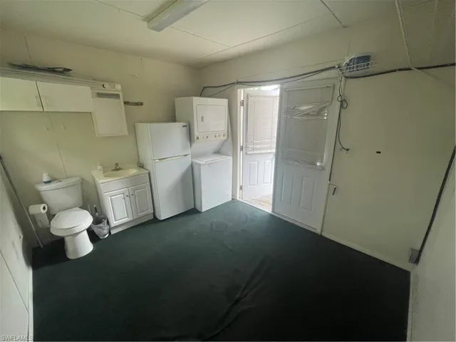 Bathroom featuring stacked washer and clothes dryer, toilet, and vanity