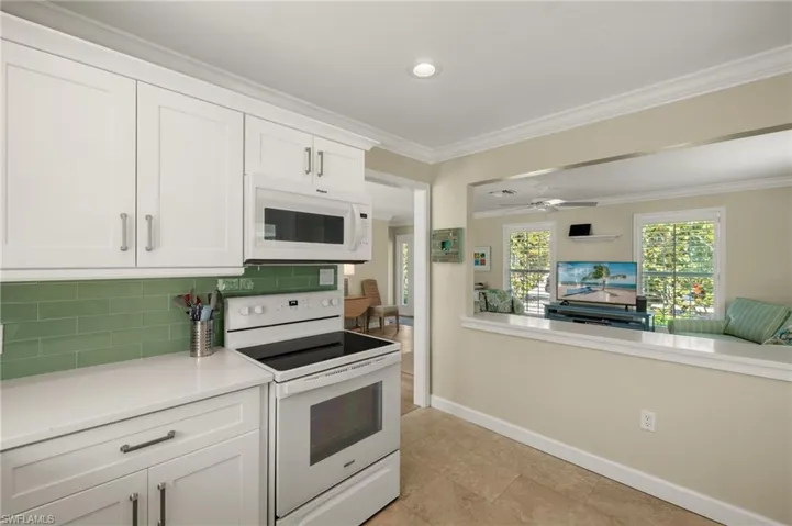 Kitchen featuring white appliances, decorative backsplash, light countertops, crown molding, and white cabinetry
