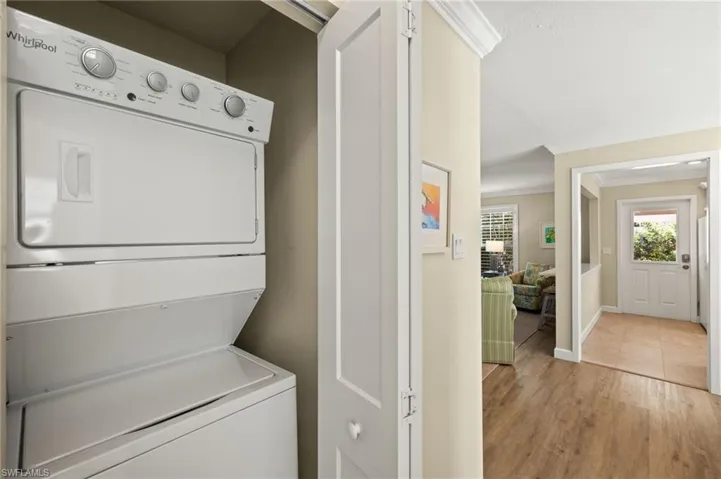 Washroom with light wood-style flooring, laundry area, stacked washer / dryer, baseboards, and ornamental molding
