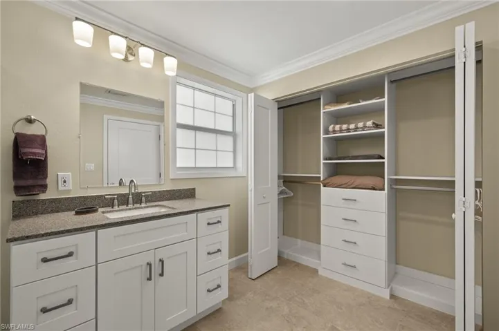 Bathroom with a walk in closet, vanity, and crown molding