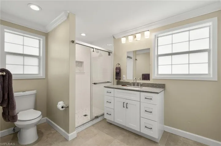 Bathroom featuring toilet, ornamental molding, a stall shower, and a wealth of natural light