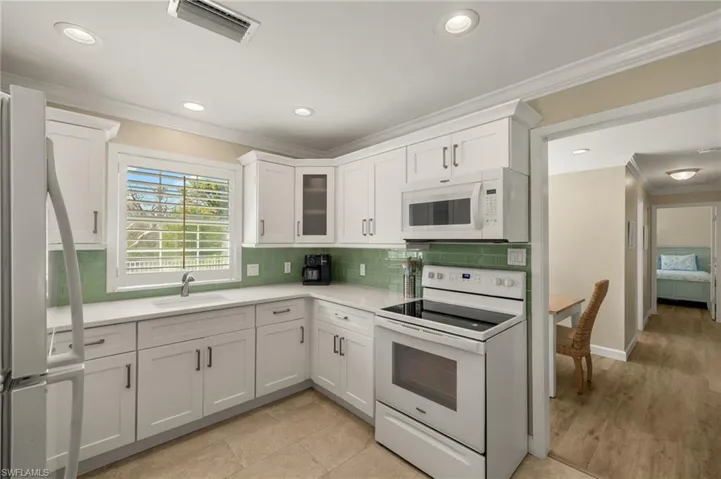 Kitchen with ornamental molding, light countertops, white appliances, and a sink