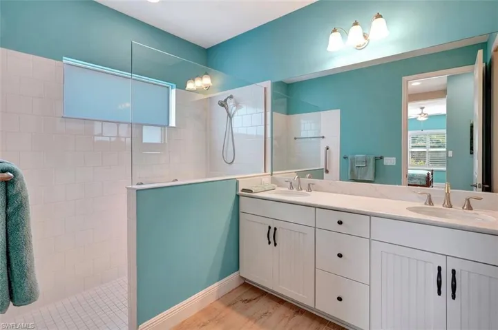Master bathroom with quartz counter tops, walk-in shower, planked flooring, wainscoted cabinetry & tiled shower floor.