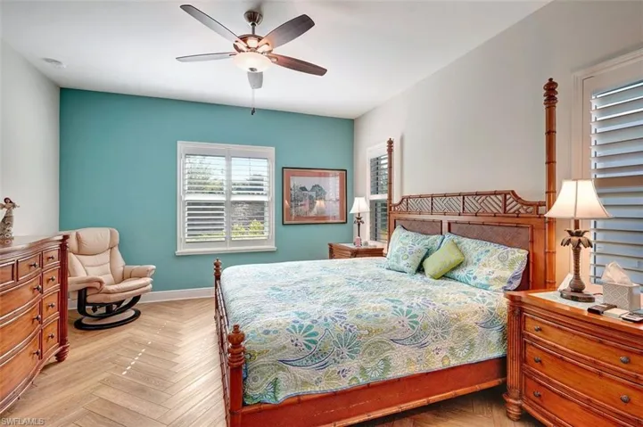The master bedroom is a retreat with planked flooring, new furniture, paintings, ample room, lamps & plantation shutters.