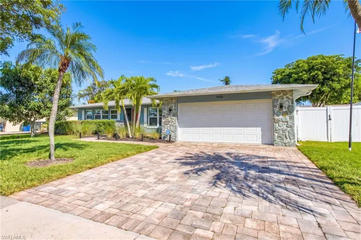 Single-story residence featuring a paved driveway, exterior stone masonry accents, a white vinyl privacy fence, and integrated garage lighting