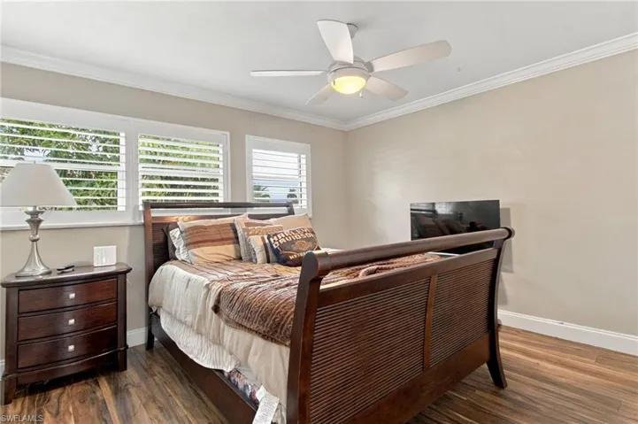Room featuring wood-finish flooring, white plantation shutters, crown molding, and a ceiling fan with integrated light fixture