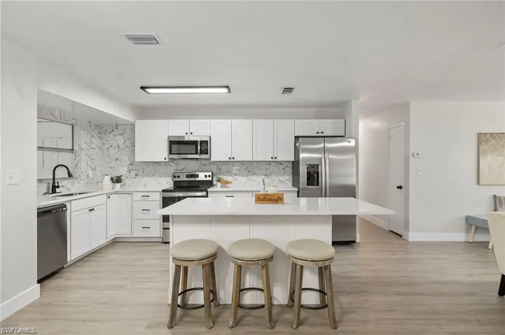 Kitchen with stainless steel appliances, a kitchen bar, a center island, and light wood finished floors