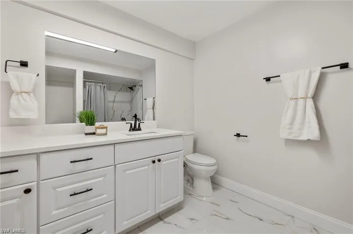 Full bath featuring curtained shower, vanity, and light marble finish floors