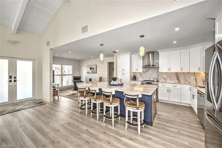 Kitchen featuring appliances with stainless steel finishes, decorative light fixtures, white cabinetry, a center island, and wall chimney range hood