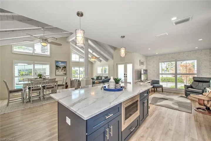 Kitchen featuring hanging light fixtures, light hardwood / wood-style flooring, stainless steel microwave, a kitchen island, and light stone countertops