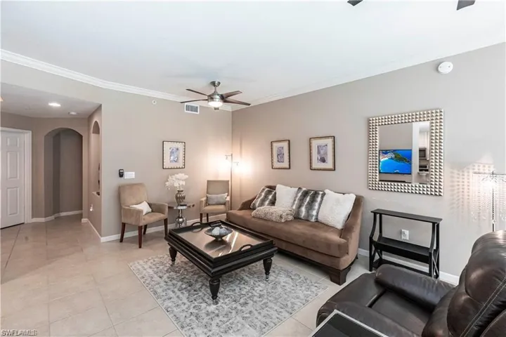 Living room with arched walkways, a ceiling fan, light tile patterned flooring, and ornamental molding