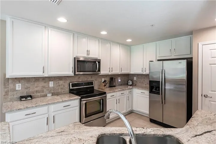 Kitchen with stainless steel appliances, white cabinets, light stone counters, light tile patterned floors, and recessed lighting