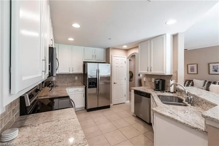Kitchen featuring stainless steel appliances, decorative backsplash, light stone counters, white cabinetry, and light tile patterned flooring