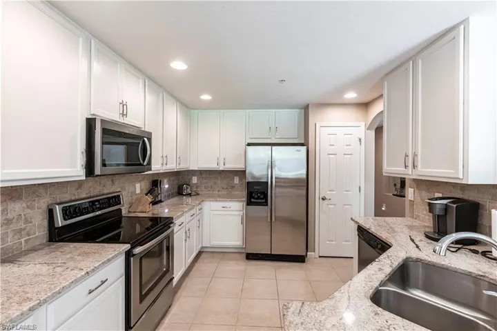 Kitchen featuring stainless steel appliances, light stone countertops, white cabinets, light tile patterned flooring, and recessed lighting