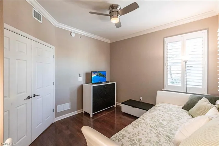 Bedroom with dark wood-style floors, crown molding, and a ceiling fan