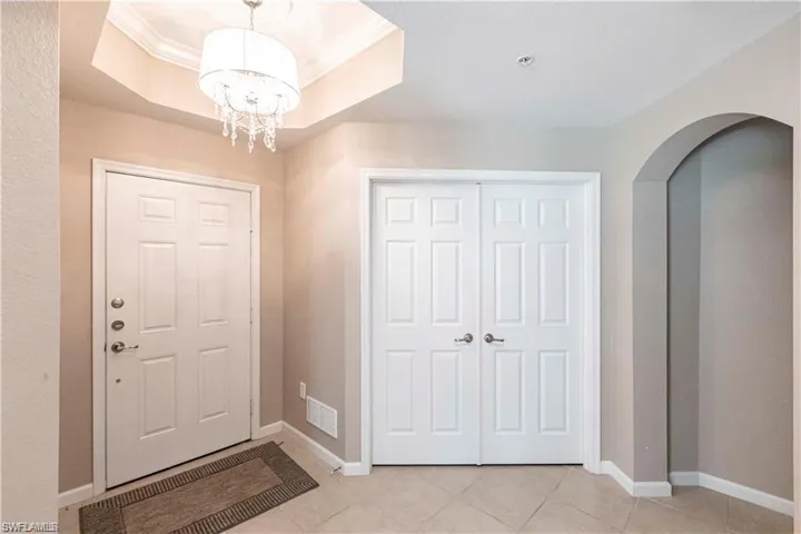 Foyer featuring light tile patterned flooring, ornamental molding, arched walkways, a raised ceiling, and a chandelier