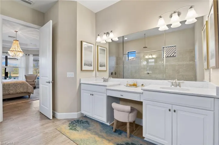 Ensuite bathroom with double vanity, walk in shower, light wood-style floors, and hanging lights
