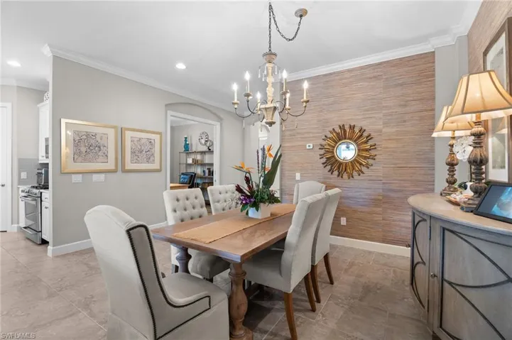 Dining space featuring crown molding, a chandelier, arched walkways, and an accent wall